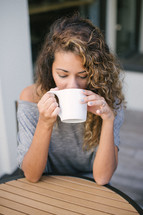 woman sitting at a table outdoors drinking coffee 