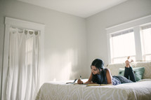 A teen girl studying while laying on a bed.