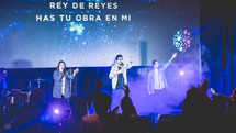 worship leaders performing on stage in front of a projection screen with Spanish lyrics 