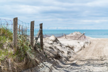 A fence next to sand dunes and a blue ocean.