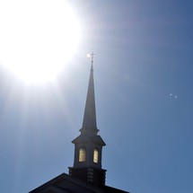 glowing sun over a steeple against a blue sky 