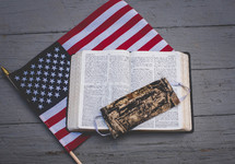 camouflaged mask on the pages of an opened Bible on an American Flag 