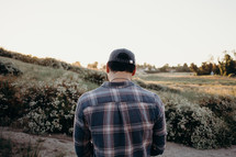 a man in a plaid shirt walking in tall grass on a hill 