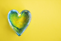 green glass heart on yellow background 