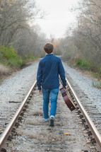 a man with a guitar walking on train tracks 