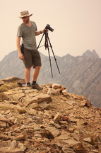 a man holding a camera on top of a mountain 