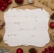 Christmas ornaments around a white wood sign 