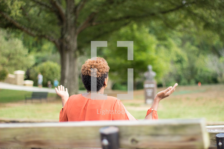a woman sitting on a park bench with raised hands praying to God 