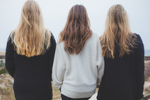 Three women with long hair standing together and looking away.
