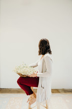 a woman sitting on a stool with a basket of picked daisies 