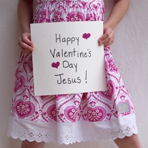 A little girl holding up a sign that reads Happy Valentine's day Jesus 