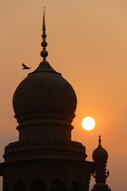 Bird flying over Islamic Mosque at sunset.