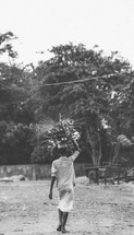 a woman in a village balancing items on her head 