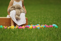 toddler girl with a stuffed bunny and Easter eggs in grass 