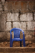 broken plastic chair in front of a stone wall 