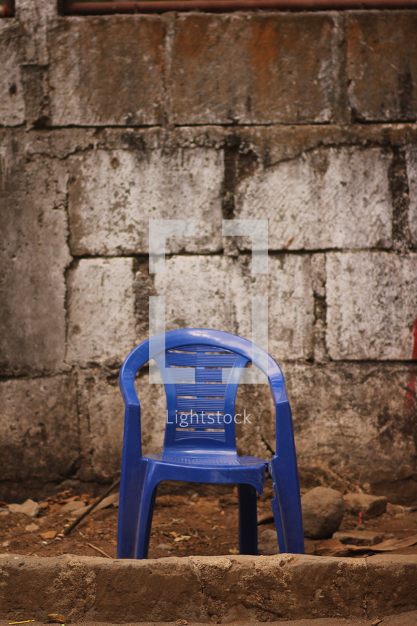 broken plastic chair in front of a stone wall 