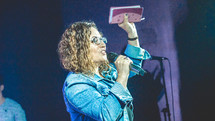 a woman holding a microphone and a raised Bible during a worship service 
