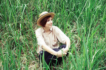 a woman in a straw hat sitting in tall grasses 