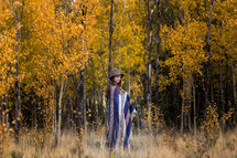 a young woman wrapped in a blanket standing in a fall forest 