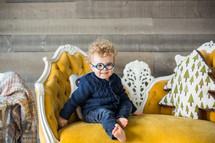a toddler in glasses sitting on a couch 