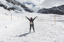 a woman with raised hands standing on a snowy mountain 