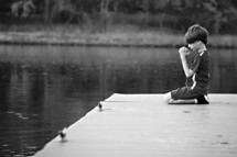 boy child kneeling in prayer on a dock 