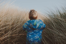 a toddler in a coat walking through tall grasses 
