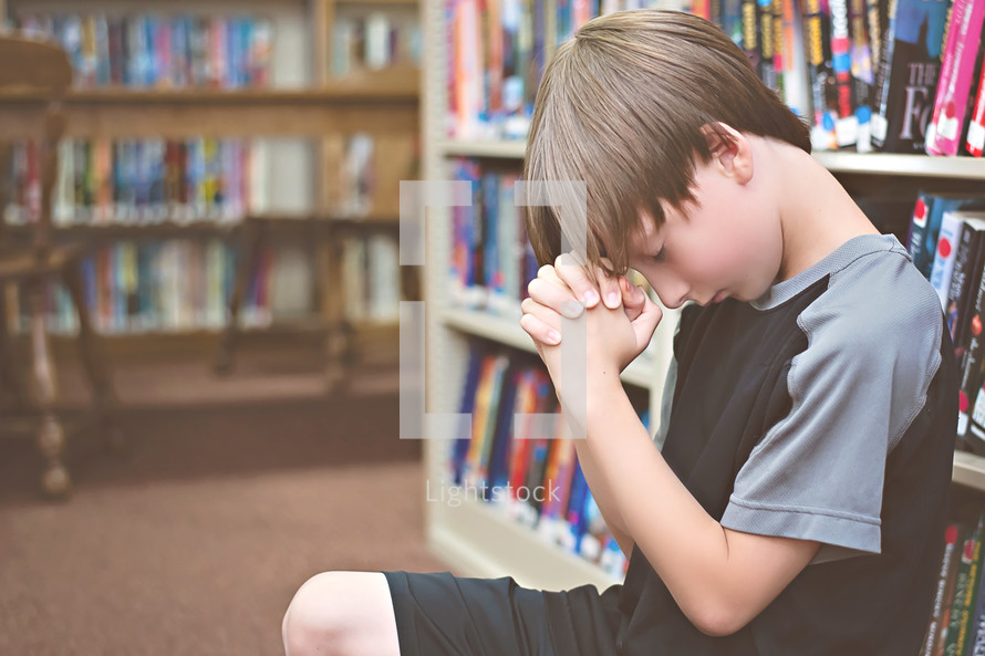 boy child praying in a library