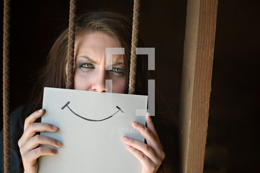 woman hiding behind a smiley face picture, behind bars 