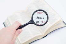 Hand holding magnifying glass over Bible text "Jesus."