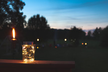 flames on a tiki torch and fairy lights in a jar on a railing 