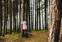a girl in a raincoat hugging a tree 