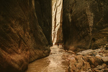 woman walking through a river at the bottom of a canyon 