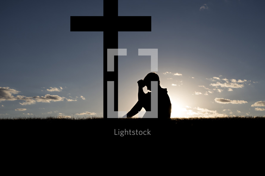 silhouette of a boy sitting under a cross in prayer