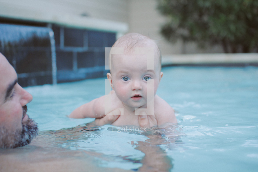 a father and infant son swimming in a pool 