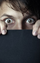 eyes of a man peeking over a black board 
