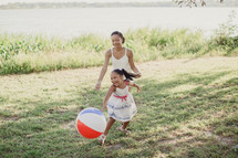 A young woman and little girl playing outdoors with a beach ball.