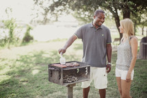 A man talking to a woman while grilling hamburgers and hot dogs.