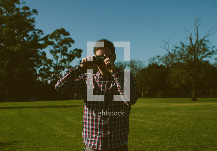 man in a plaid shirt taking a picture with a camera 