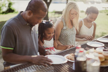 family holding hands in prayer sitting at a picnic table 