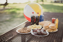 hamburgers and hotdogs on a table outdoors with a beach ball 