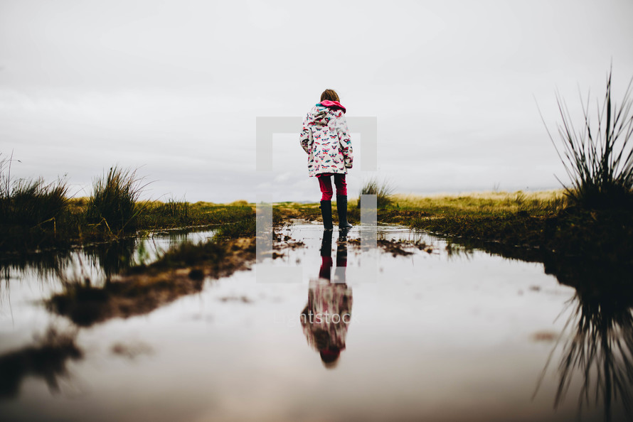 a girl in rainbows and a rain coat walking through a puddle 