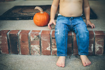 a toddler boy sitting on a porch with pumpkins 