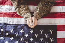 military man with praying hands over an American flag 
