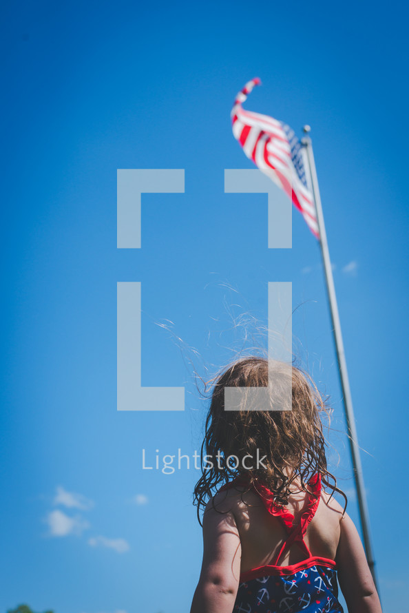 little girl looking up at an American flag on a flagpole 