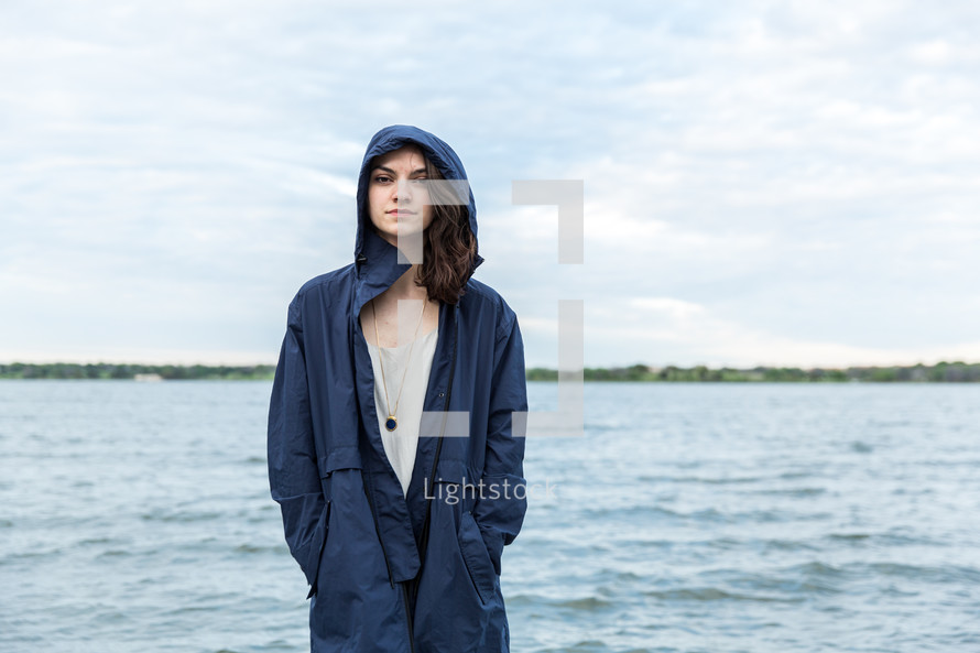 young woman standing by water in a hooded jacket 