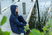 young woman in a hoodie sitting on a wood pier 