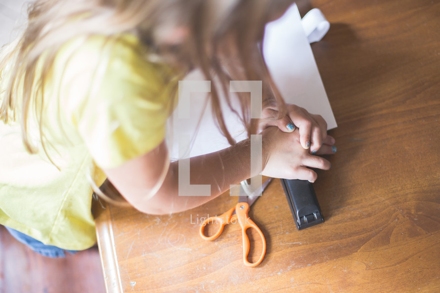 A young girl stapling a sheet of paper.