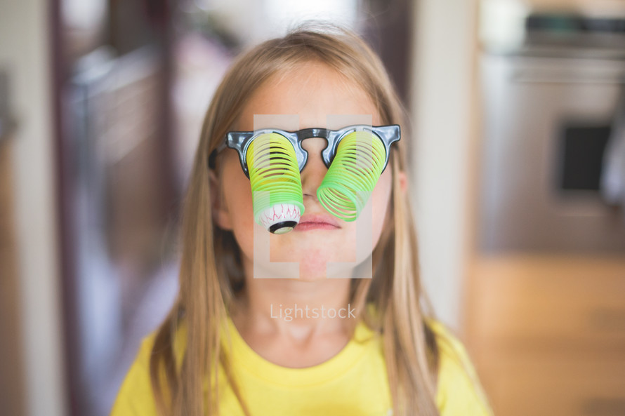 Young girl wearing toy glasses with dangling google eyes.