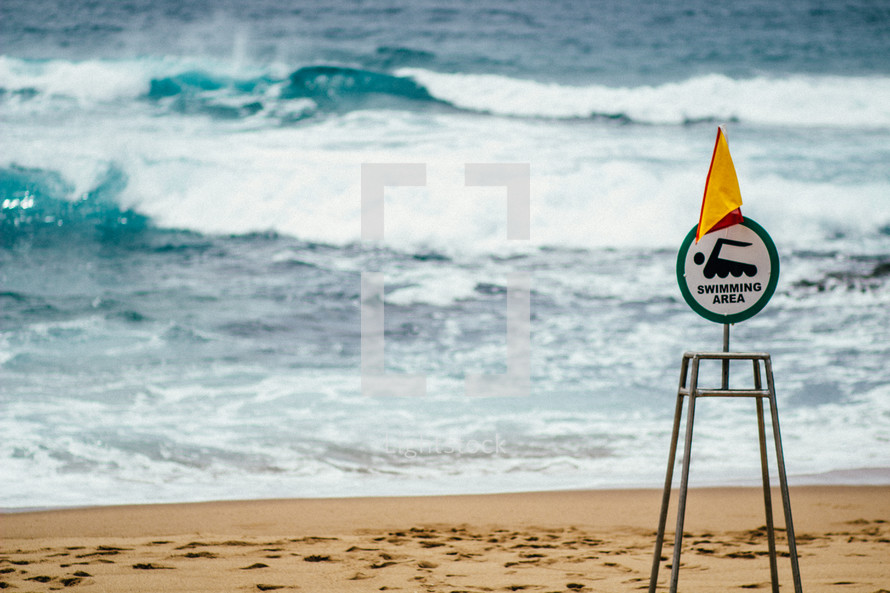 A sign on a beach by the ocean denoting that it is a swimming area.